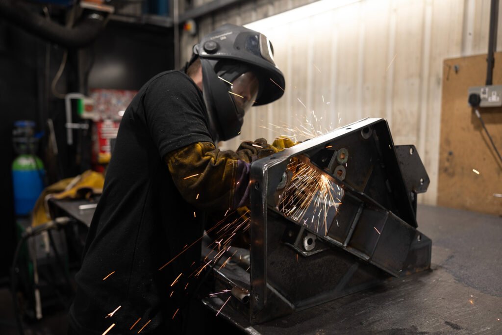 man wearing PPE performing a linishing job on a large metal fabrication