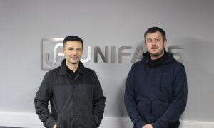 Jarek Gasiorek, Production Director (left), congratulates Krystian on 10 years of service in sheet metal fabrication as a Press brake operator and powder coating supervisor at Unifabs Ltd. Both stand in front of a Unifabs logo sign cut from sheet metal on a grey wall