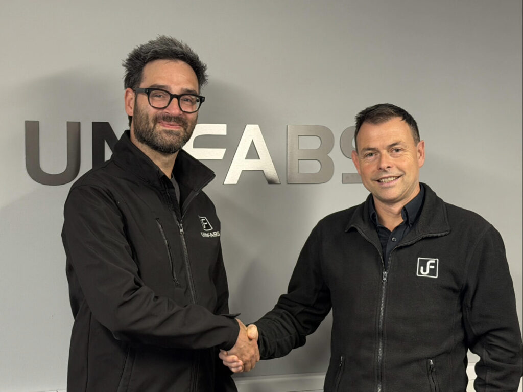 Gary Moreton achieves 10 years' service milestone at UK sheet Metal Fabricator Unifabs Ltd. Pictured with Andy Tuck shaking hands in front of a Unifabs sign on a grey wall.